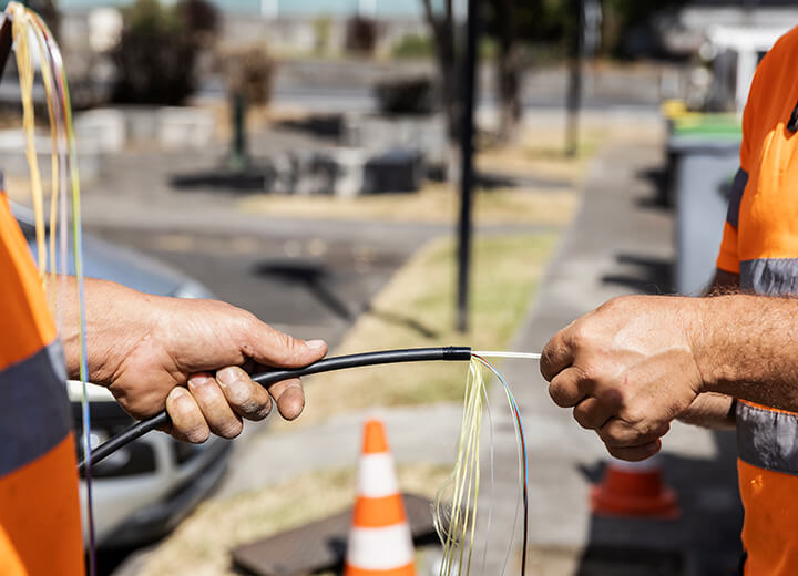 Deux techniciens en tenue de chantier tiennent un câble de fibre optique ouvert lors d’une intervention sur un réseau télécom