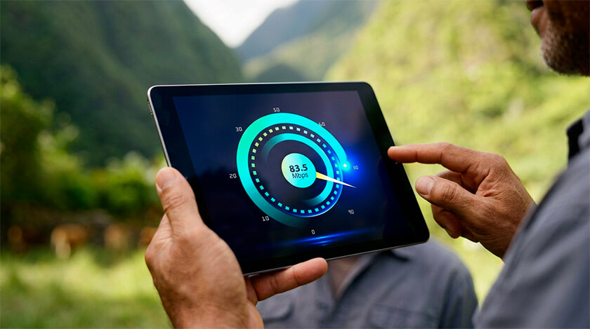 Une personne tient une tablette affichant un test de vitesse internet à 83,5 Mbps, avec un paysage montagneux en arrière-plan.