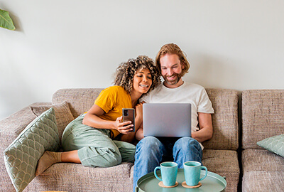 Couple détendu assis sur un canapé, regardant un ordinateur portable ensemble avec deux tasses sur une table basse