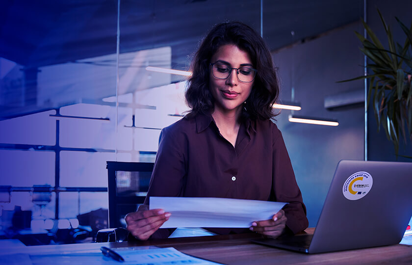 Professionnelle consultant des documents administratifs devant un ordinateur portable, illustrant la gestion des données, le travail numérique et la cybersécurité en entreprise