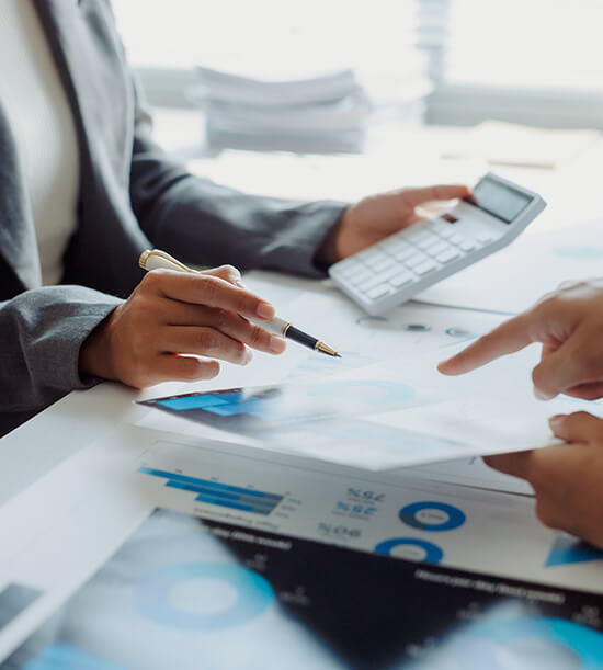 Gros plan sur deux personnes examinant des graphiques financiers et des documents, avec une calculatrice posée sur la table.